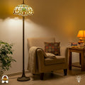 Tiffany vloerlamp Barok verlicht in woonkamer — naast beige fauteuil met deken en kussen, groene plant links, bijzettafel met boeken rechts