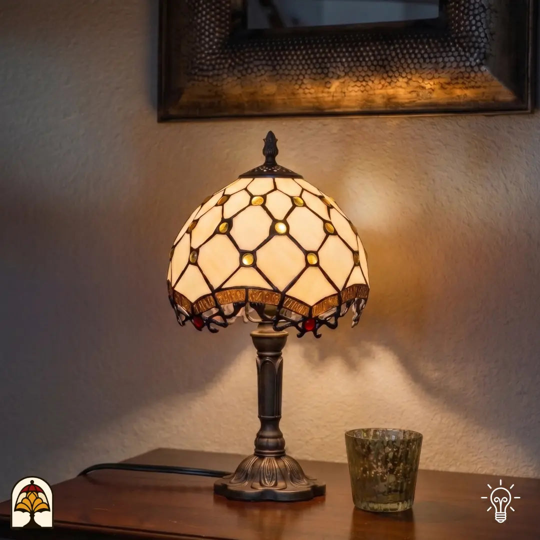 Verlichte Tiffany lamp tafellamp Reticolo d'Oro ⌀20 cm in interieur op houten tafel – crème kap met gouden juwelen en diamantpatroon, bronzen voet, warm licht