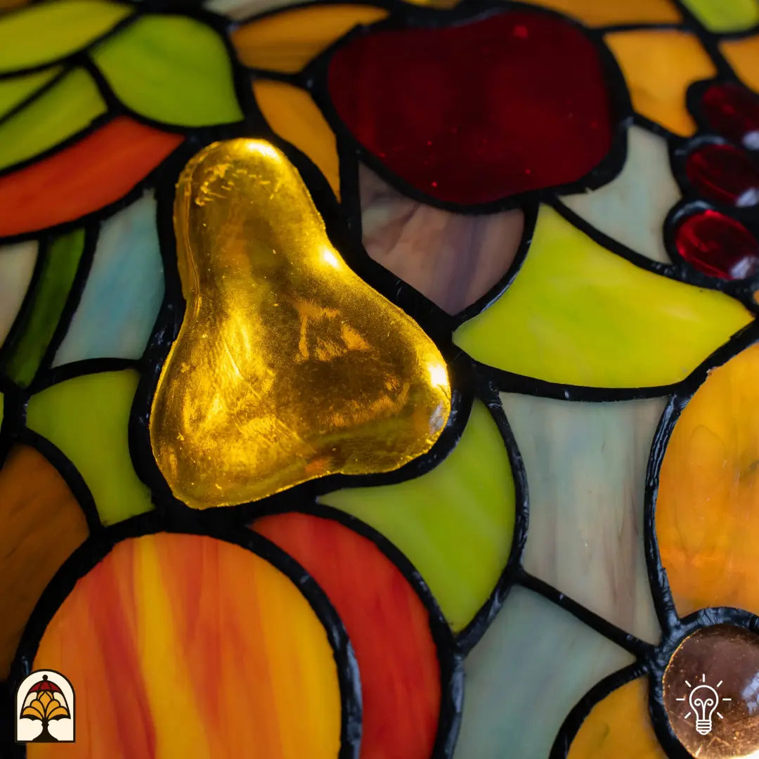 Detail kap Tiffany tafellamp Frutta Viva — goudkleurige peer in glas centraal, rode appel en paarse druiven rondom, groene bladeren