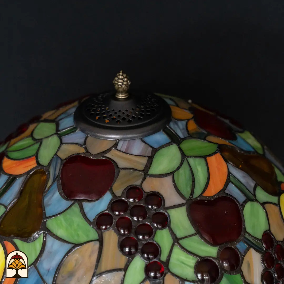Close-up bovenkant kap Tiffany tafellamp Frutta Viva — geperforeerd ventilatierooster, fruitmotief met rode appels en druiven rondom, groene bladeren