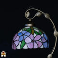 Close-up onverlichte Tiffany kap — blauw/paarse en roze bloemen op witte achtergrond, groene bladeren, rode edelsteentjes