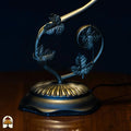Close-up voet — donkere gebogen arm met bladvormige decoraties, ovale ronde basis met geribbeld goud/brons patroon, aansluitsnoer zichtbaar