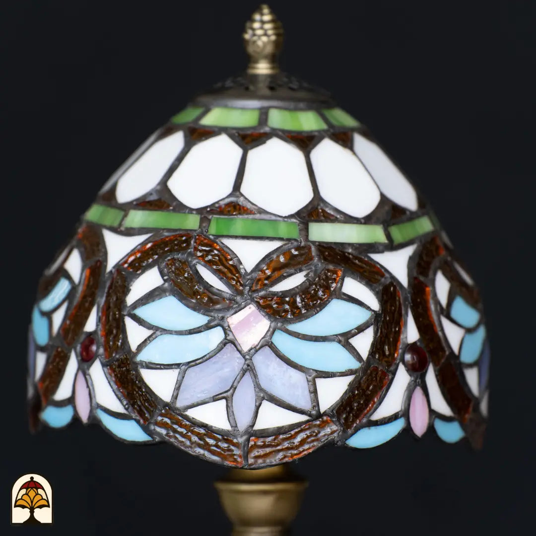 Close-up onverlichte koepelkap Tiffany tafellamp Lucette – wit glas met groene sierband, bruine bladvormen, lichtblauwe en roze bloemblaadjes en rode edelsteen