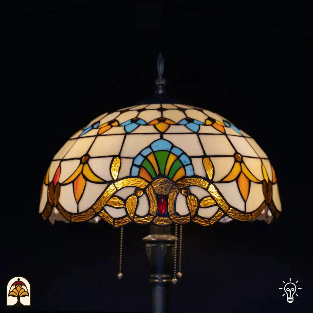 Close-up verlichte kap Tiffany vloerlamp Barok — crème/amber glas, centrale blauwe boog met groene waaier, rode edelsteen op bronzen rand, trekschakelaar