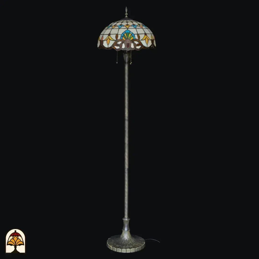 Close-up verlichte kap Tiffany vloerlamp Barok van voren — crème/amber glas met blauw/groen centraal motief, gele en oranje bladvormige elementen, barokse bronzen onderrand