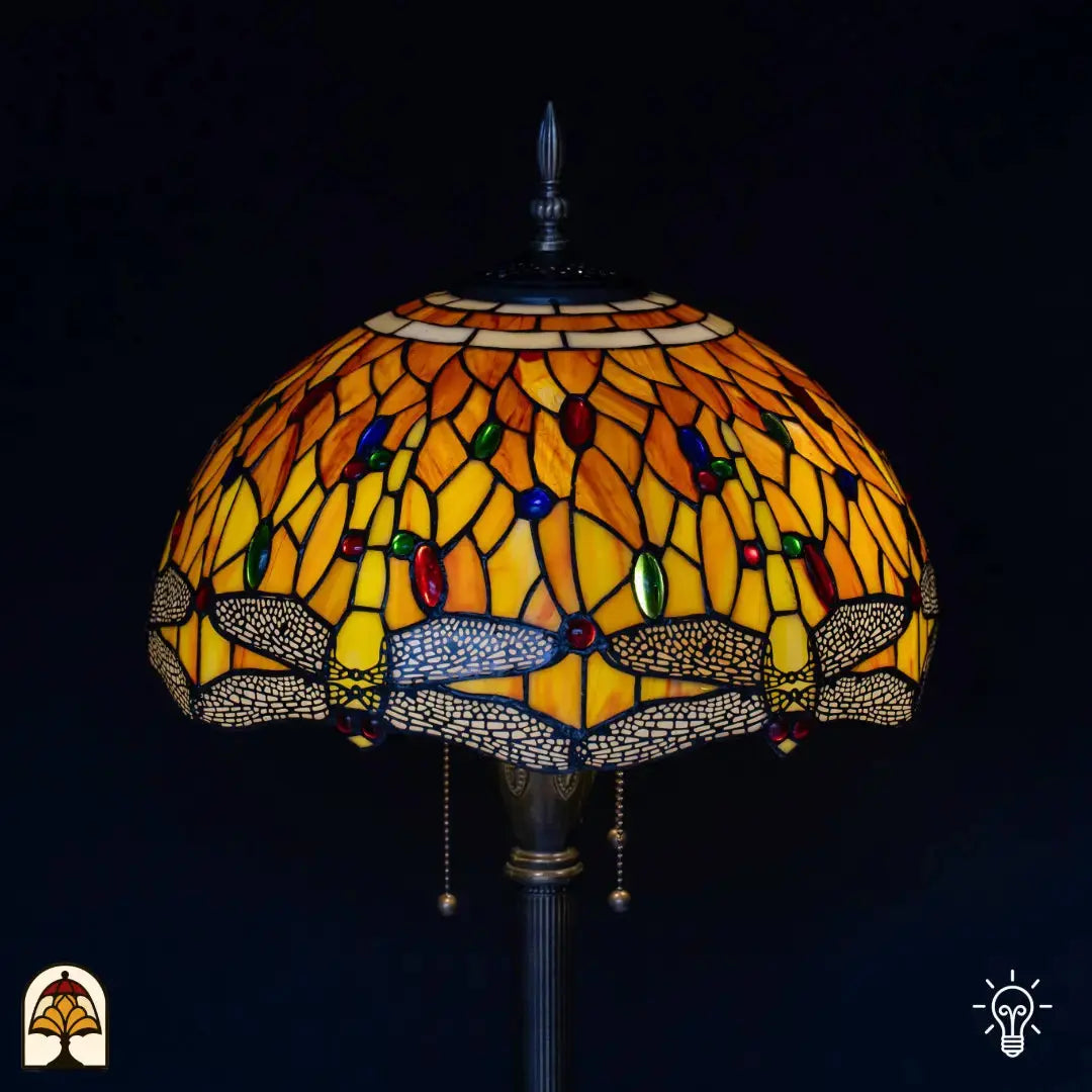 Close-up verlichte kap Tiffany vloerlamp Libellula Aurea — amber/geel/oranje glas met libellenmotief in grijze rand, rode en groene edelstenen, trekschakelaars