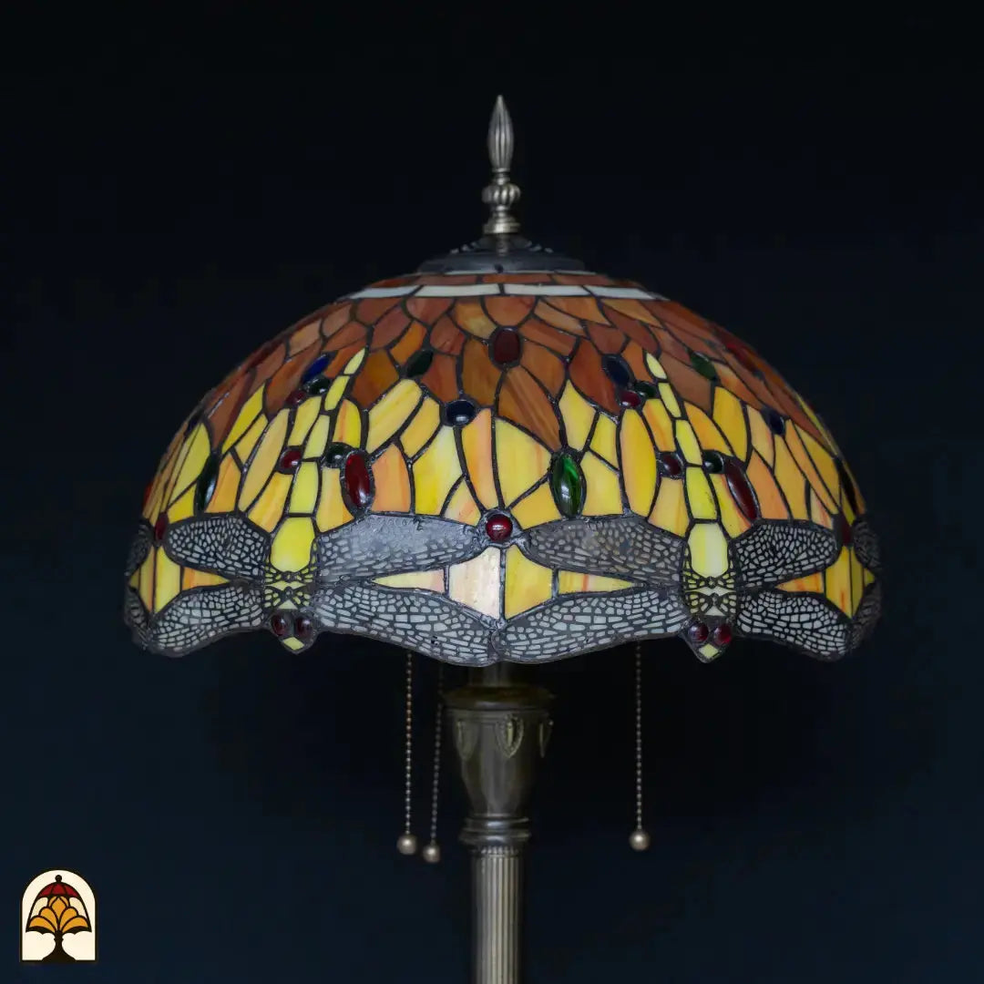Close-up kap Tiffany vloerlamp Libellula Aurea onverlicht — geel/oranje/amber glas met rode, blauwe en groene edelstenen, grijze libellenrand onderaan