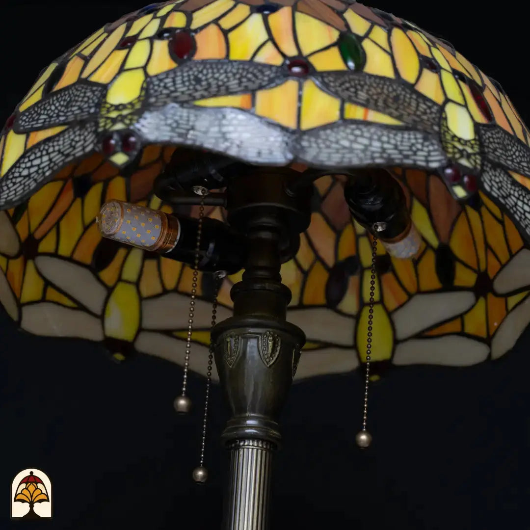 Close-up fitting Tiffany vloerlamp Libellula Aurea onverlicht — twee LED-peertjes in bronzen fitting, trekschakelaars, kleurrijke kap met libellenrand op achtergrond