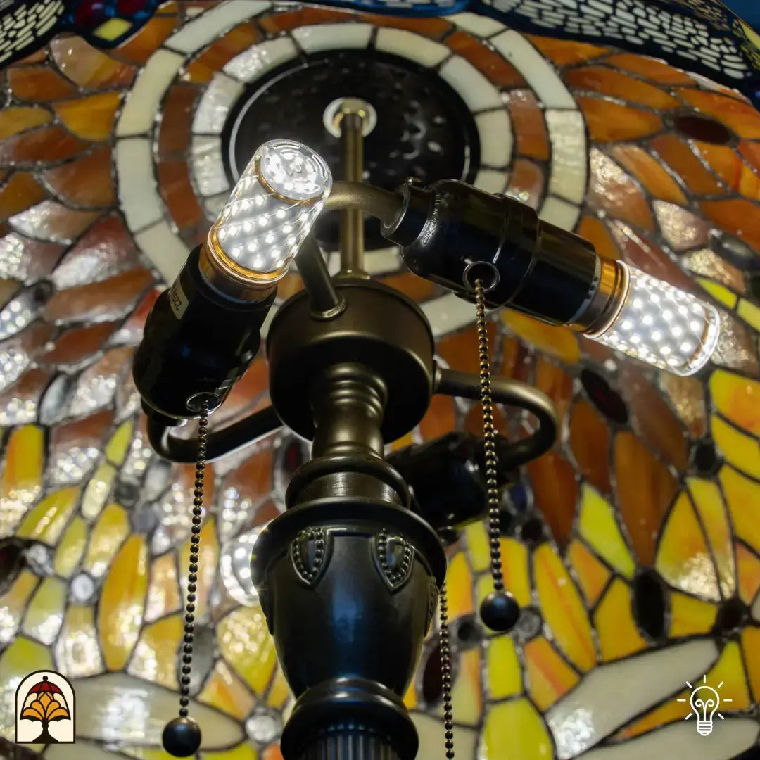 Close-up verlichte fitting Tiffany vloerlamp Libellula Aurea van onderen — twee brandende LED-peertjes in bronzen dubbele fitting, trekschakelaars, amber/geel glas verlicht rondom
