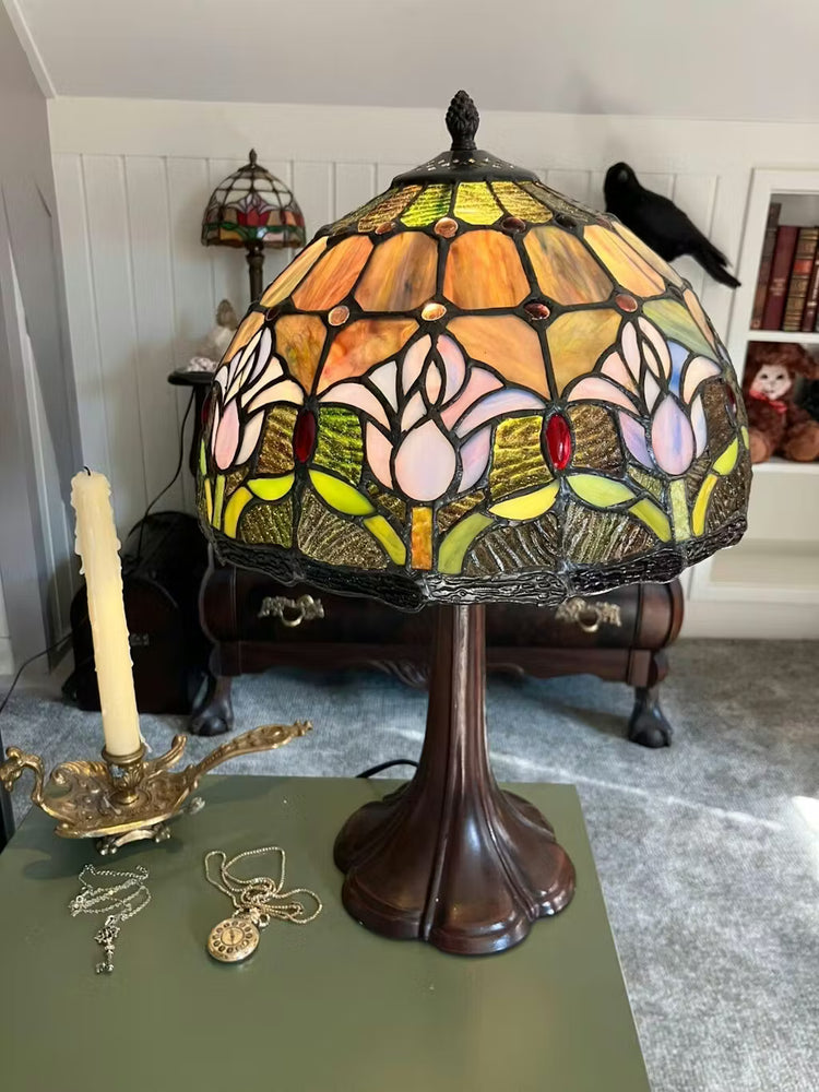 Tiffany tafellamp met paarse tulpen en groen glas-in-lood, geeft warm en sfeervol licht in een klassiek interieur.